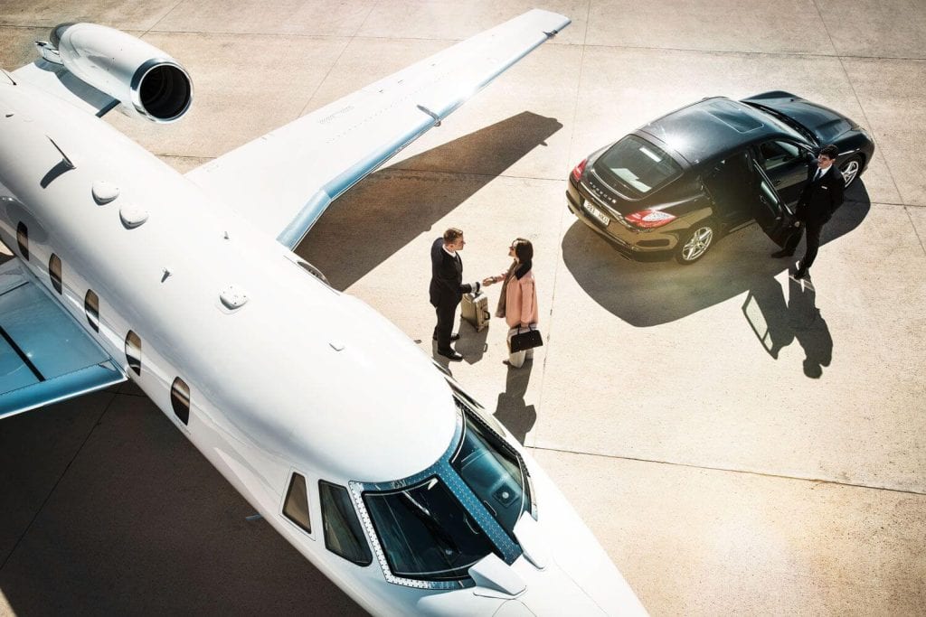 Professional chauffeur greeting clients beside a luxury car and private jet